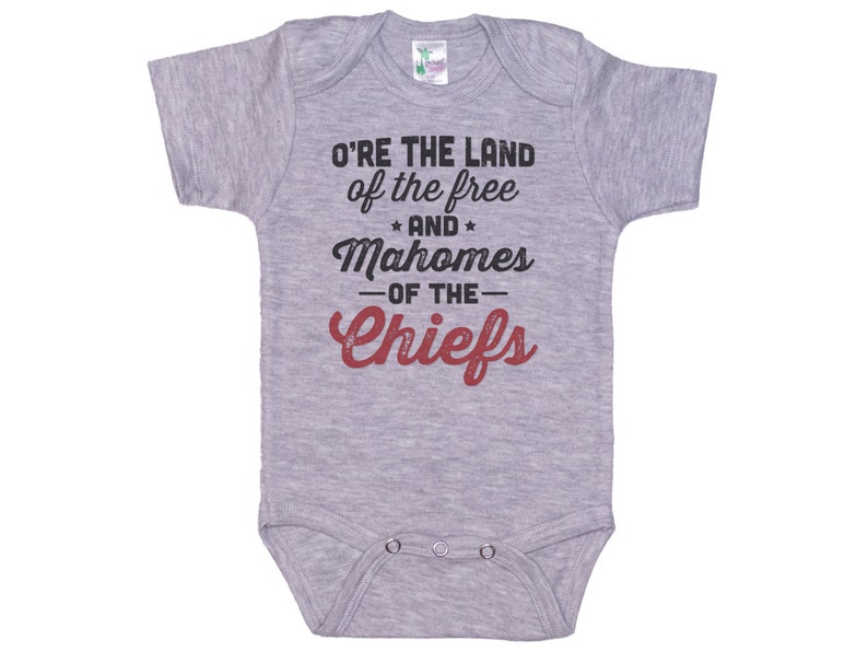 Pode incluir: Macac&atilde;o de beb&ecirc; cinza com o texto "O're the land of the free and Mahomes -of the- Chiefs" em preto e vermelho.