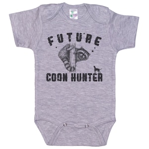 May include: Gray baby onesie with black text that reads "FUTURE COON HUNTER" and a black and white illustration of a raccoon and a dog.