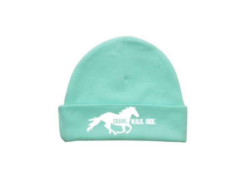 May include: A light green beanie with a white silhouette of a horse running and the text "CRAWL WALK RIDE".