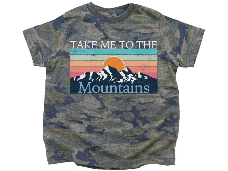 May include: A camouflage green t-shirt with a vintage-style graphic of mountains and a sunset. The text on the shirt reads "Take Me To The Mountains".
