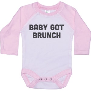 May include: White long-sleeve baby onesie with pink sleeves and a black graphic that says "BABY GOT BRUNCH".