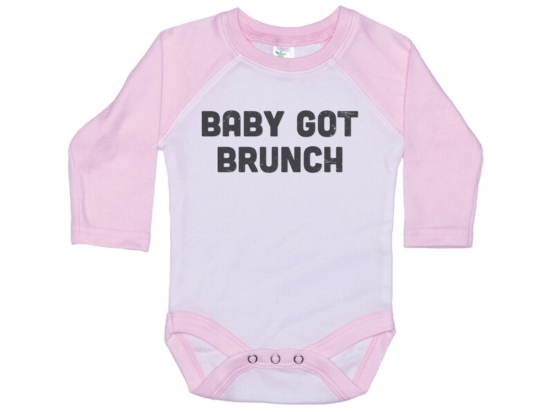 May include: White long-sleeve baby onesie with pink sleeves and a black graphic that says "BABY GOT BRUNCH".