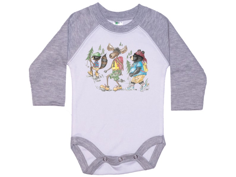 May include: A white long-sleeve baby bodysuit with a grey raglan sleeve design. The bodysuit features a cartoon illustration of a moose, a raccoon, and a bear wearing backpacks and hiking in the woods.