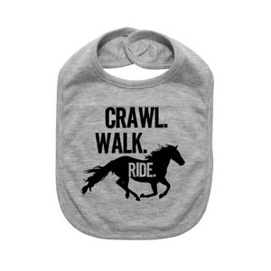May include: A gray baby bib with the words "Crawl. Walk. Ride." in black block letters. A black silhouette of a running horse is below the text. The bib has a rounded shape and a snap closure.