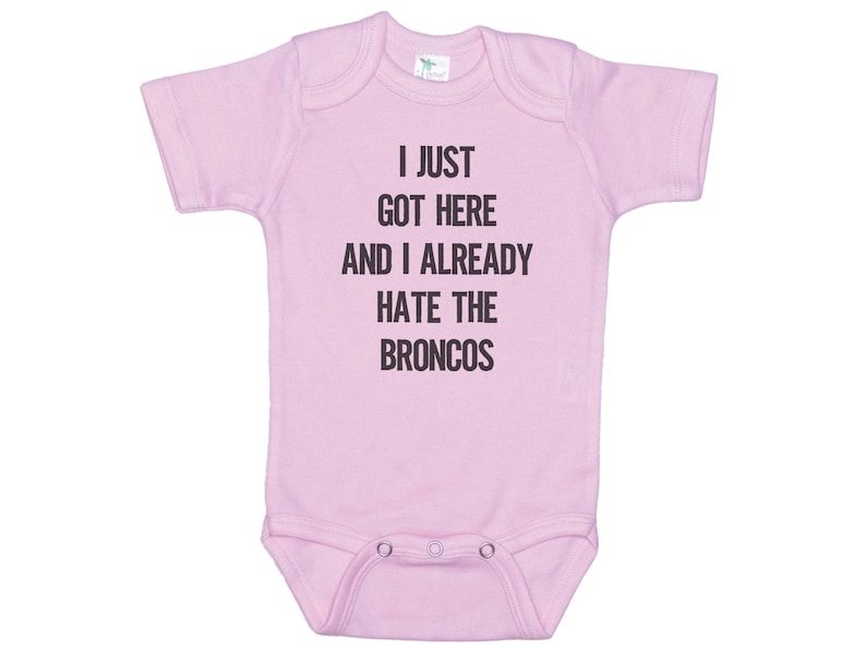 May include: Pink baby onesie with the text "I just got here and I already hate the Broncos" printed in black.