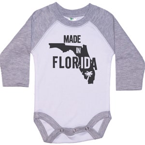 K&ouml;nnte beinhalten: Wei&szlig;er und grauer Langarm-Babybody mit einer schwarzen Umrandung des Bundesstaates Florida und dem Text "MADE IN FLORIDA".