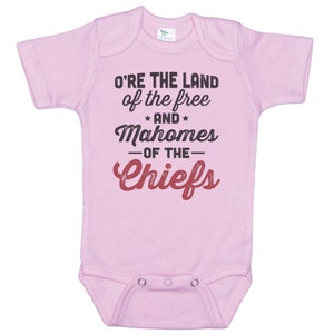 Pode incluir: Macac&atilde;o rosa para beb&ecirc; com o texto "O're the land of the free and Mahomes -of the- Chiefs" em preto e vermelho.
