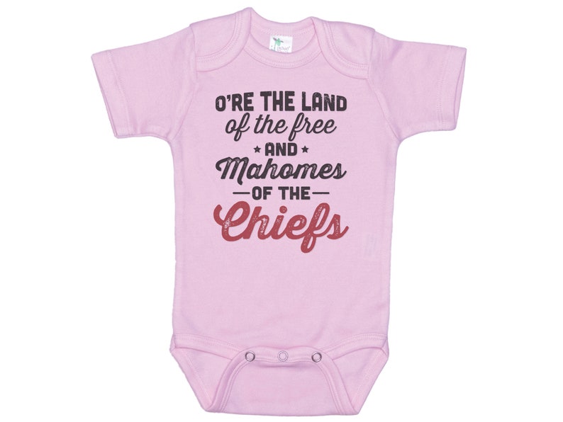 Pode incluir: Macac&atilde;o rosa para beb&ecirc; com o texto "O're the land of the free and Mahomes -of the- Chiefs" em preto e vermelho.
