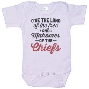 Pode incluir: Macac&atilde;o branco para beb&ecirc; com mangas curtas e um gr&aacute;fico vermelho e preto que diz "O're the land of the free and Mahomes -of the- Chiefs".