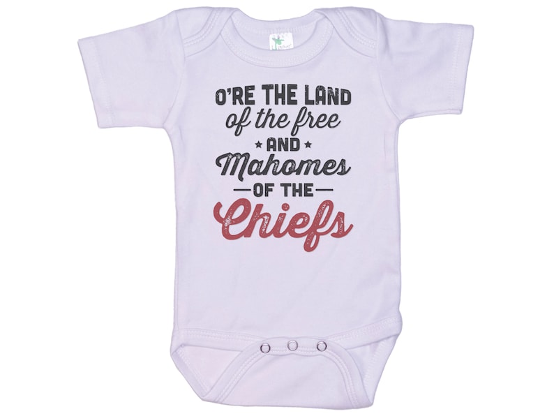 Pode incluir: Macac&atilde;o branco para beb&ecirc; com mangas curtas e um gr&aacute;fico vermelho e preto que diz "O're the land of the free and Mahomes -of the- Chiefs".