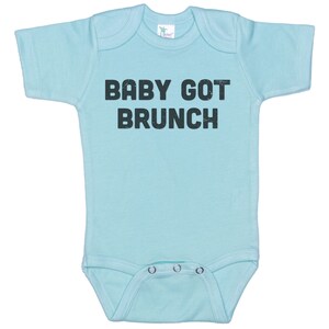 May include: A light blue baby onesie with short sleeves and a black print that says "BABY GOT BRUNCH".
