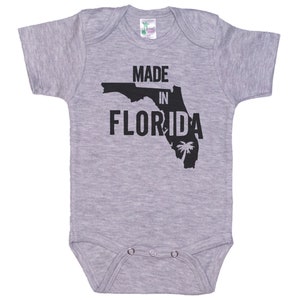 K&ouml;nnte beinhalten: Grauer kurz&auml;rmeliger Baby-Strampler mit einer schwarzen Umrandung des Bundesstaates Florida und dem Text "Made in Florida".