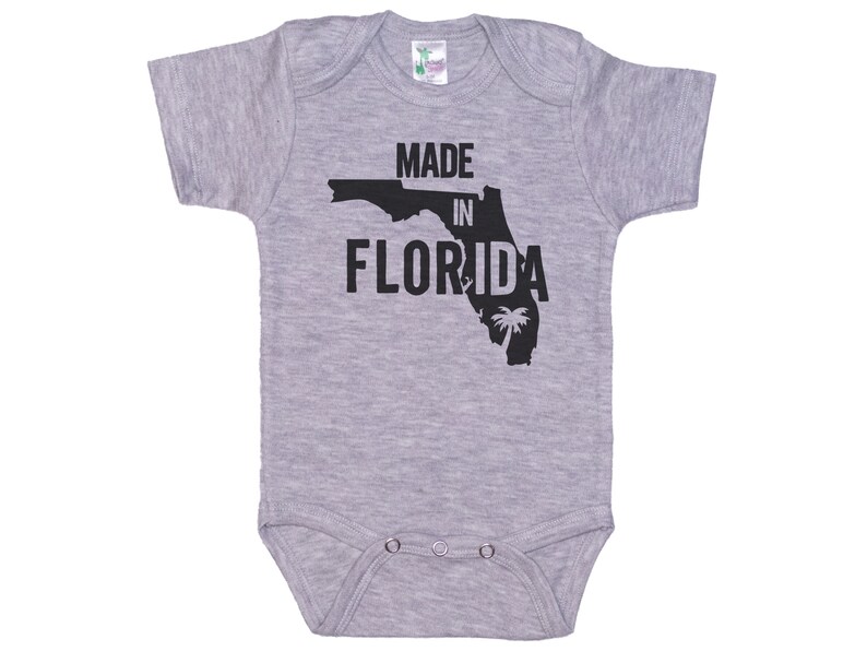 K&ouml;nnte beinhalten: Grauer kurz&auml;rmeliger Baby-Strampler mit einer schwarzen Umrandung des Bundesstaates Florida und dem Text "Made in Florida".