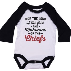Pode incluir: Macac&atilde;o branco de manga comprida para beb&ecirc; com mangas pretas. O macac&atilde;o tem um gr&aacute;fico vermelho e preto que diz "O're the land of the free and Mahomes -of the- Chiefs".
