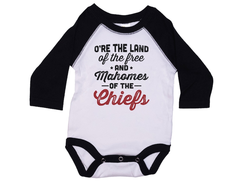 Pode incluir: Macac&atilde;o branco de manga comprida para beb&ecirc; com mangas pretas. O macac&atilde;o tem um gr&aacute;fico vermelho e preto que diz "O're the land of the free and Mahomes -of the- Chiefs".
