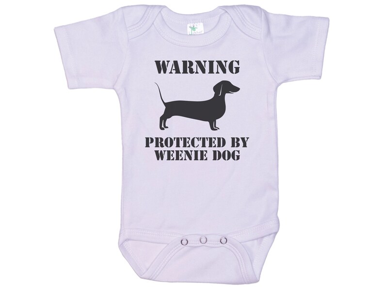 May include: White baby onesie with black text that reads "WARNING PROTECTED BY WEENIE DOG" and a black silhouette of a dachshund.
