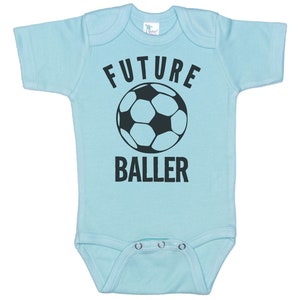 May include: A light blue baby onesie with a black soccer ball and the text "FUTURE BALLER" printed on the front.