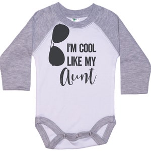 May include: A white and gray long-sleeve baby bodysuit with a black graphic of sunglasses and the text "I'm cool like my Aunt".
