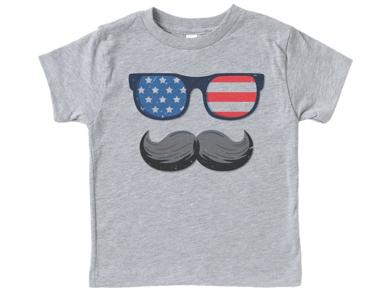 May include: A grey t-shirt with a graphic of sunglasses with a blue frame and the American flag design on the lenses, and a grey moustache. The sunglasses have a blue frame with white stars on one lens and red and white stripes on the other. The moustache is grey.