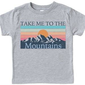 May include: A heather grey t-shirt with a vintage-style graphic of a mountain range with a setting sun and the text "Take Me To The Mountains".