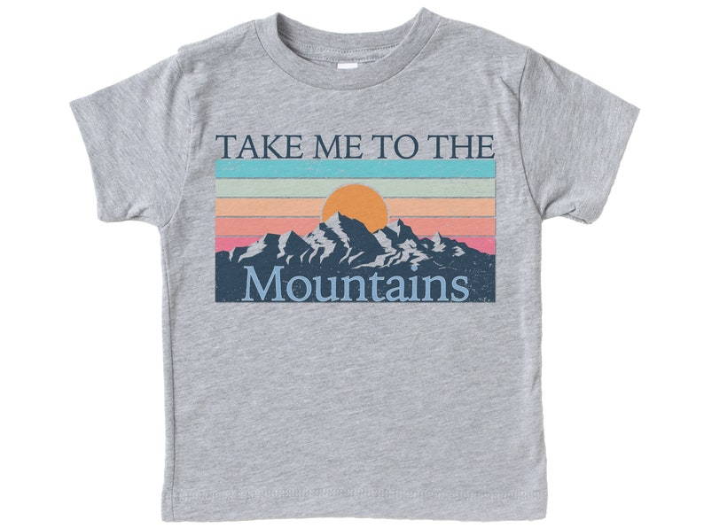 May include: A heather grey t-shirt with a vintage-style graphic of a mountain range with a setting sun and the text "Take Me To The Mountains".
