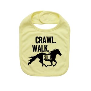 May include: A light yellow baby bib with the words "Crawl. Walk. Ride." in black block letters. A black silhouette of a running horse is below the text. The bib has a rounded shape and a snap closure.