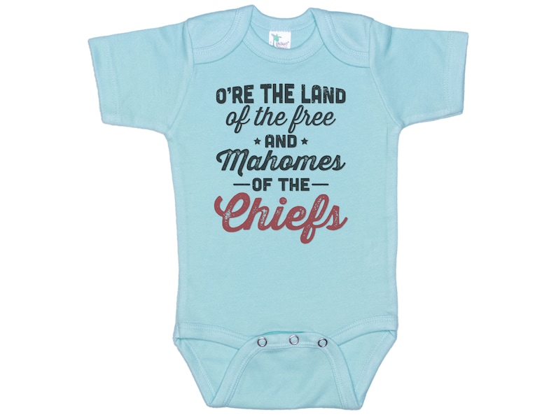 Pode incluir: Macac&atilde;o de beb&ecirc; azul claro com o texto "O're the land of the free *and* Mahomes -of the- Chiefs" em preto e vermelho.