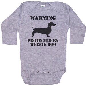 May include: Gray long-sleeve baby onesie with black text that reads "WARNING PROTECTED BY WEENIE DOG" and a black silhouette of a dachshund.