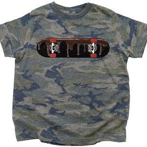 Może przedstawiać: Koszulka w kamuflaż z grafiką brązowej deski skateboardowej z czerwonymi k&oacute;łkami i kapiącą czekoladą.