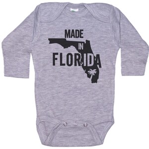 K&ouml;nnte beinhalten: Grauer Langarm-Babybody mit einer schwarzen Umrandung des Bundesstaates Florida und dem Text "MADE IN FLORIDA".