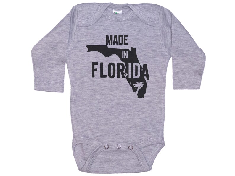 K&ouml;nnte beinhalten: Grauer Langarm-Babybody mit einer schwarzen Umrandung des Bundesstaates Florida und dem Text "MADE IN FLORIDA".