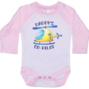 May include: A white and pink long-sleeved baby onesie with a yellow helicopter graphic and the text "Daddy's Co-Pilot".