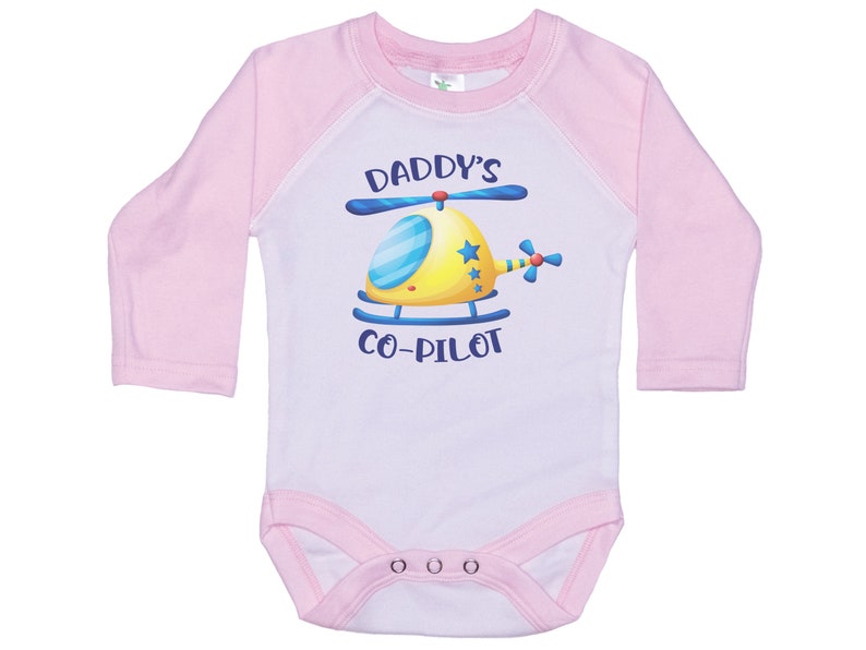 May include: A white and pink long-sleeved baby onesie with a yellow helicopter graphic and the text "Daddy's Co-Pilot".