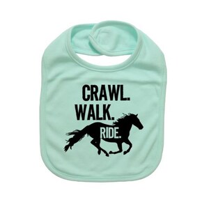 May include: A light green baby bib with the words "Crawl. Walk. Ride." in black block letters above a black silhouette of a running horse. The bib has a rounded shape and a snap closure at the neck.