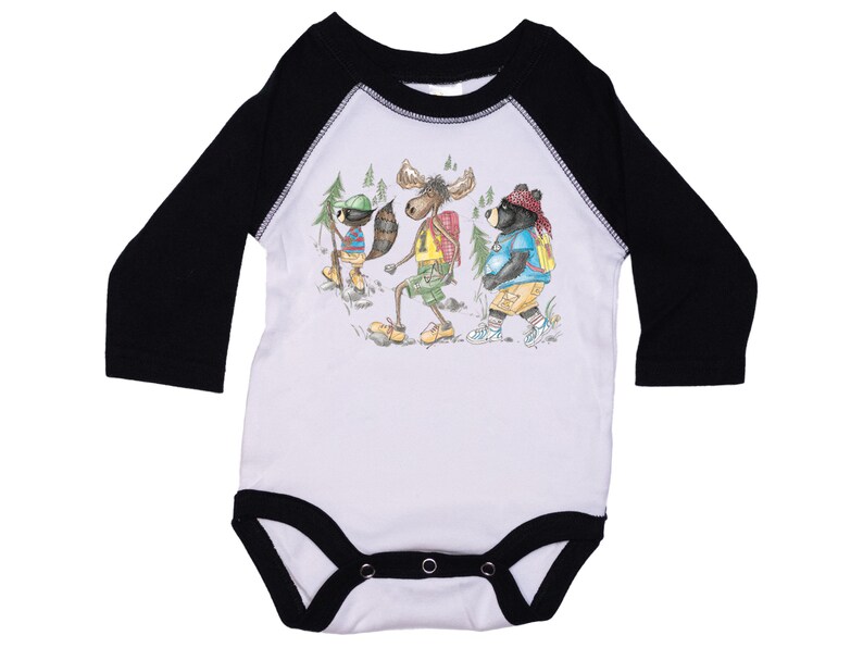 May include: White long-sleeve baby onesie with black raglan sleeves. The onesie features a graphic of a moose, a raccoon, and a bear wearing backpacks and hiking.