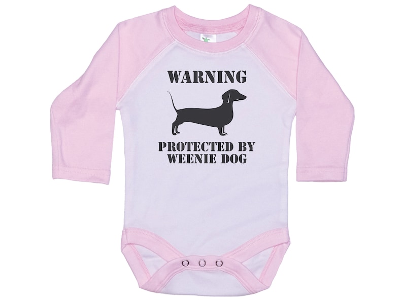 May include: A pink and white long-sleeved baby onesie with a black silhouette of a dachshund and the text "WARNING PROTECTED BY WEENIE DOG".