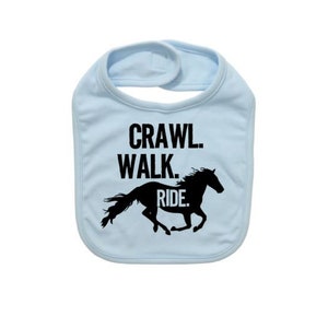 May include: A light blue baby bib with the words "Crawl. Walk. Ride." in black. A black silhouette of a horse is below the text. The bib has a hook and loop closure at the neck.