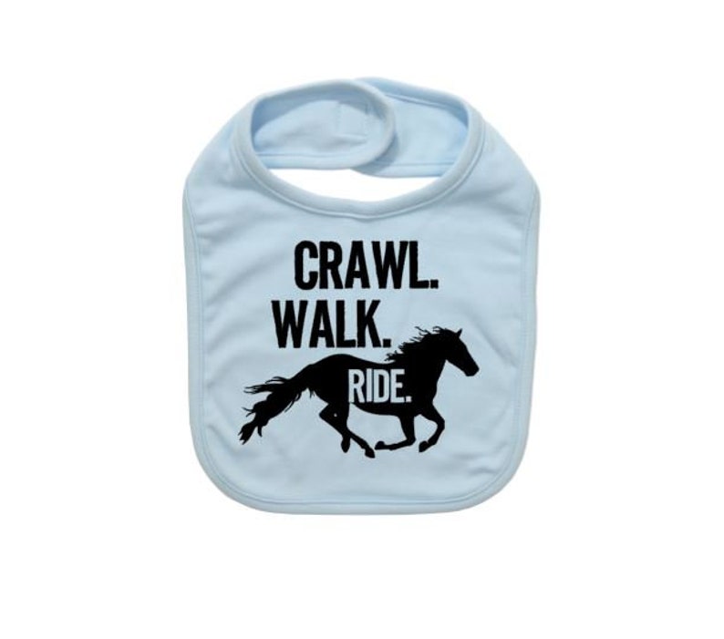 May include: A light blue baby bib with the words "Crawl. Walk. Ride." in black. A black silhouette of a horse is below the text. The bib has a hook and loop closure at the neck.
