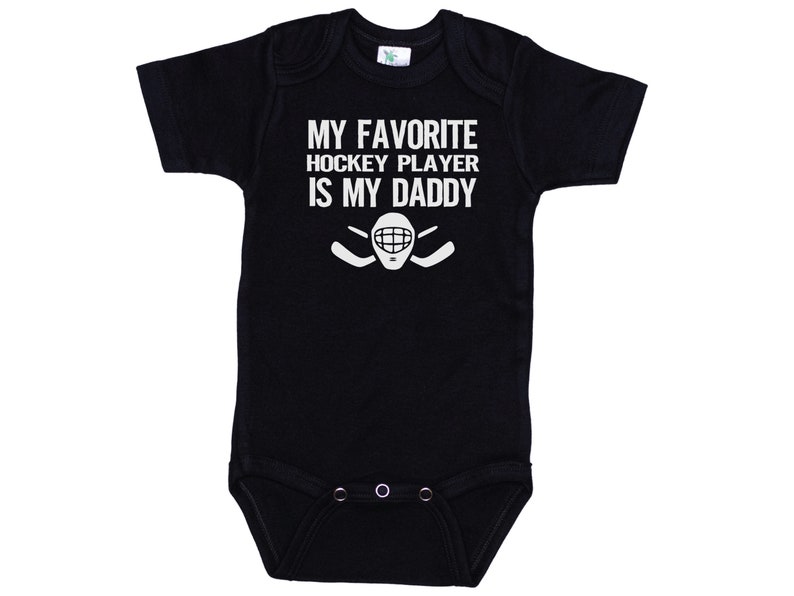 May include: Black baby onesie with white text that reads "My favorite hockey player is my daddy" with a hockey stick and goalie mask graphic.
