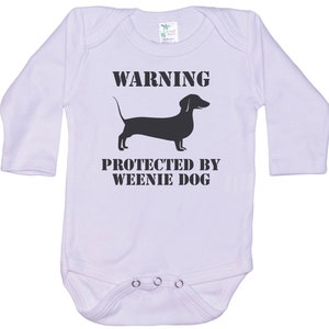 May include: White long-sleeve baby onesie with black text that reads "WARNING PROTECTED BY WEENIE DOG" and a black silhouette of a dachshund.
