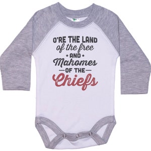Pode incluir: Macac&atilde;o de beb&ecirc; de manga comprida branco e cinza com um design estilo beisebol. O macac&atilde;o tem o texto "O'RE THE LAND of the free * AND * Mahomes -OF THE- Chiefs" em preto e vermelho.