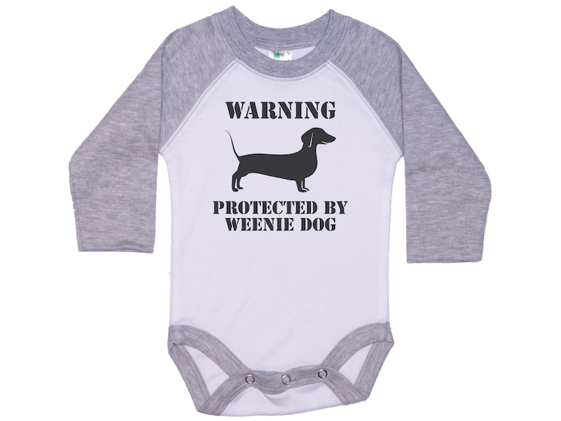 May include: A white and gray long-sleeve baby onesie with a black silhouette of a dachshund and the text "WARNING PROTECTED BY WEENIE DOG".