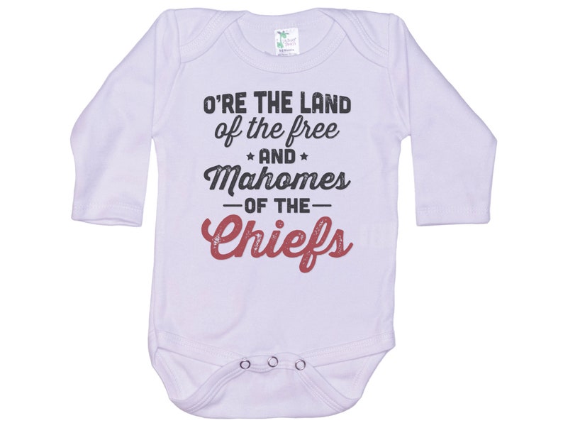 Pode incluir: Macac&atilde;o branco de manga comprida para beb&ecirc; com o texto "O're the land of the free and Mahomes -of the- Chiefs" em preto e vermelho.
