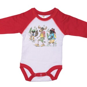 May include: White long-sleeve baby onesie with red raglan sleeves. The onesie features a graphic of a raccoon, moose, and bear wearing backpacks and hiking.