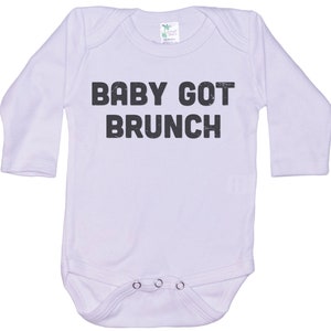 May include: White long-sleeve baby onesie with black text that reads "BABY GOT BRUNCH".