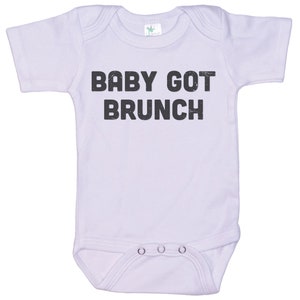 May include: A white baby onesie with short sleeves and the text "BABY GOT BRUNCH" printed in black.