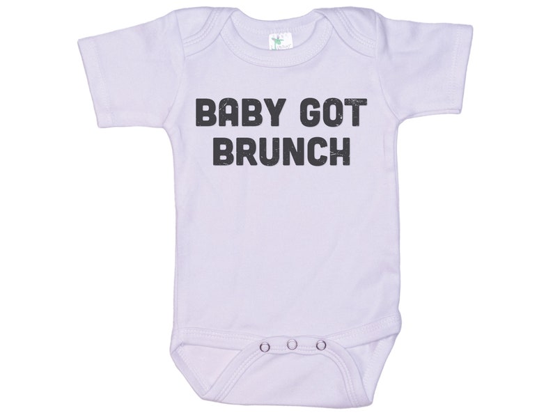 May include: A white baby onesie with short sleeves and the text "BABY GOT BRUNCH" printed in black.