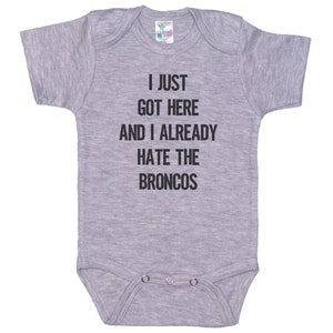 May include: Gray baby onesie with the text "I just got here and I already hate the Broncos" printed in black.
