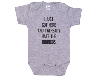 Può includere: Body per neonato grigio con il testo "I just got here and I already hate the Broncos" stampato in nero.