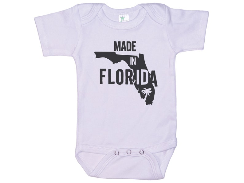 K&ouml;nnte beinhalten: Ein wei&szlig;er Baby-Strampler mit einer schwarzen Umrandung des Bundesstaates Florida und dem Text "Made in Florida".